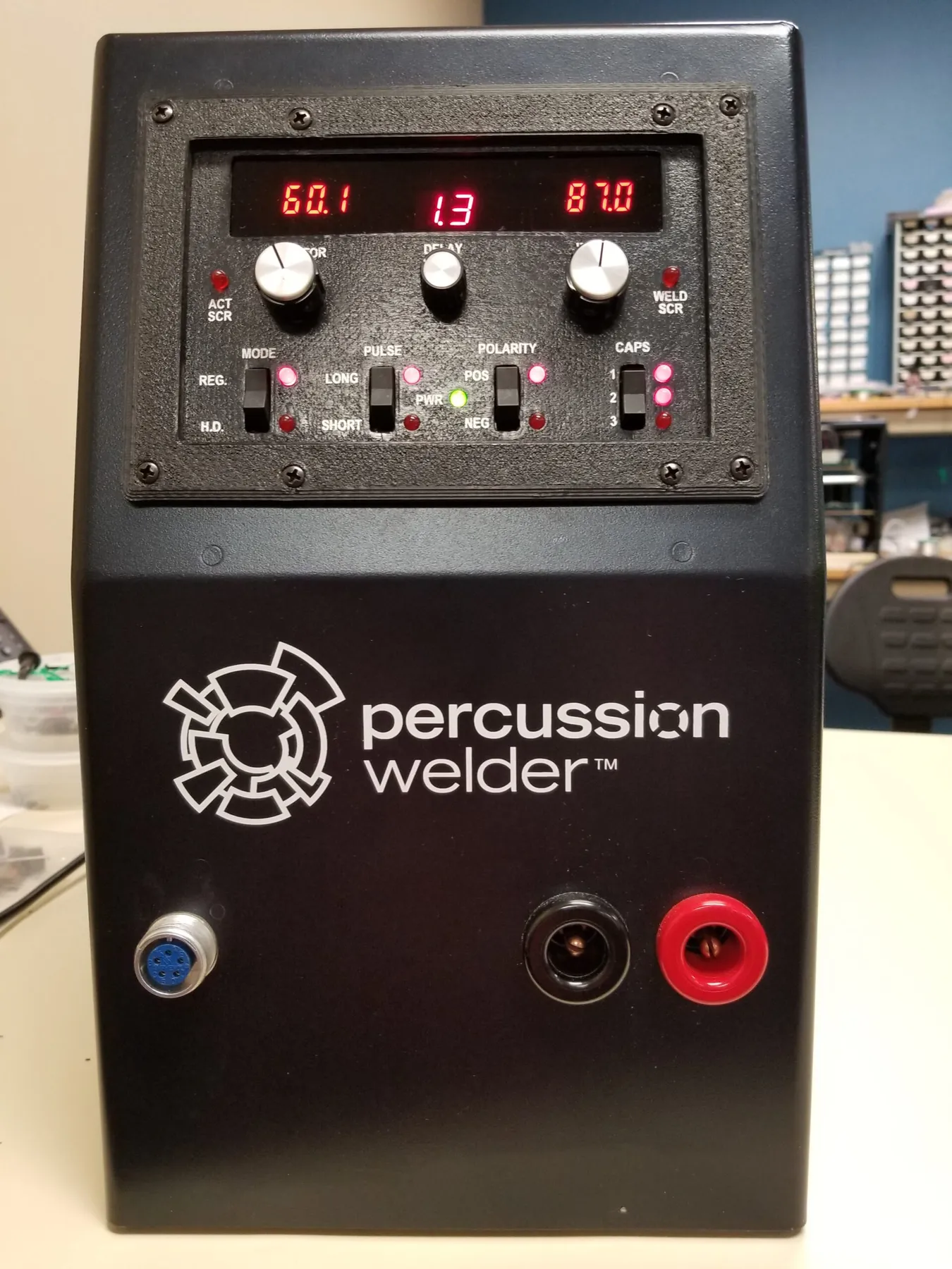 Percussion welder power supply with red digital displays on a bench, front view