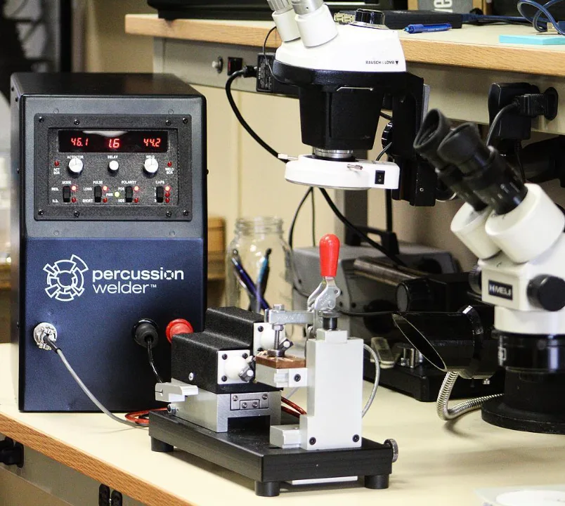 Percussion Welder 858 front panel with red readouts beside a 726 fixture and two stereo microscopes
