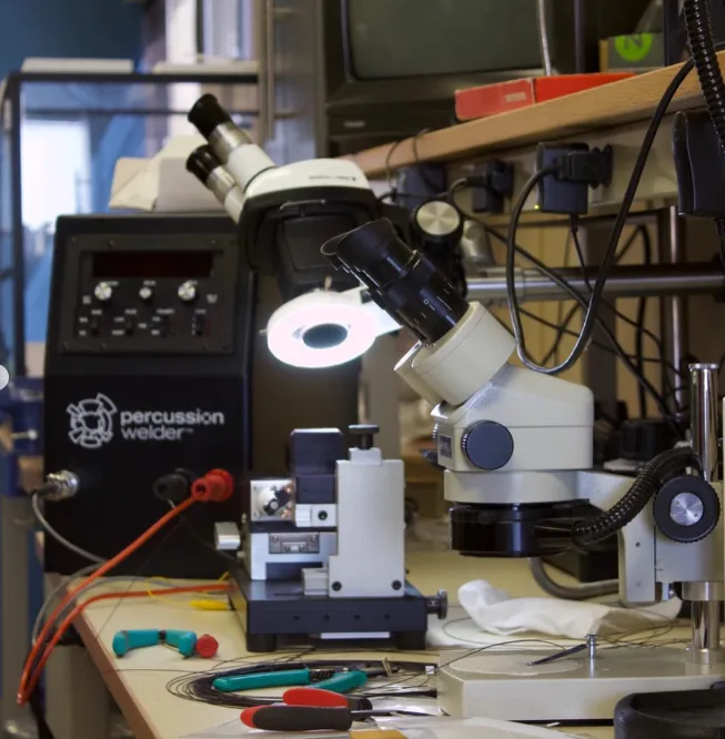 Model 858 Percussion Welder and a 726 bench fixture beside a stereo microscope with ring light on a lab bench