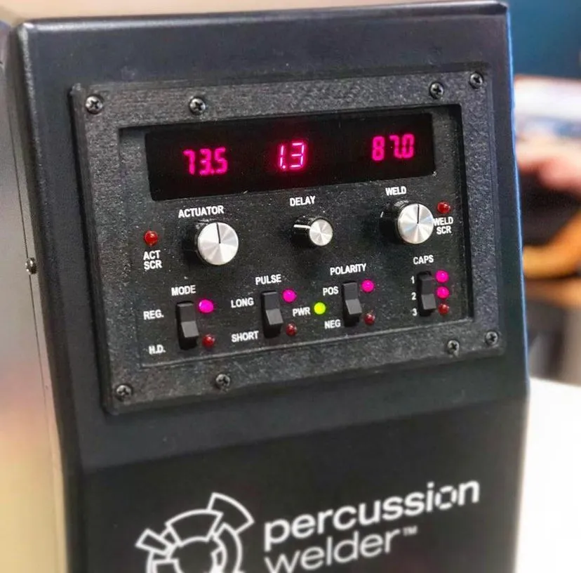 Front panel of the percussion welder with magenta-red LED readouts, dials and Percussion Welder logo