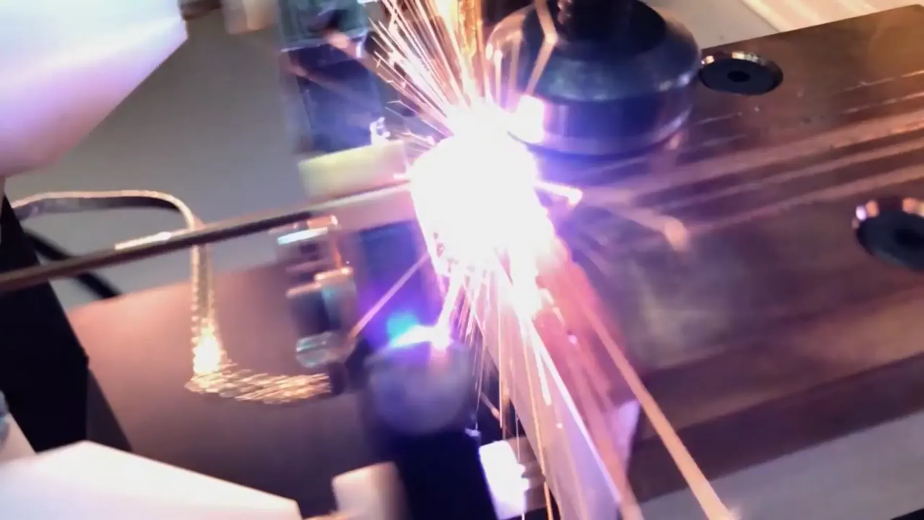 Purple-white flash and sparks at the weld point under the electrode