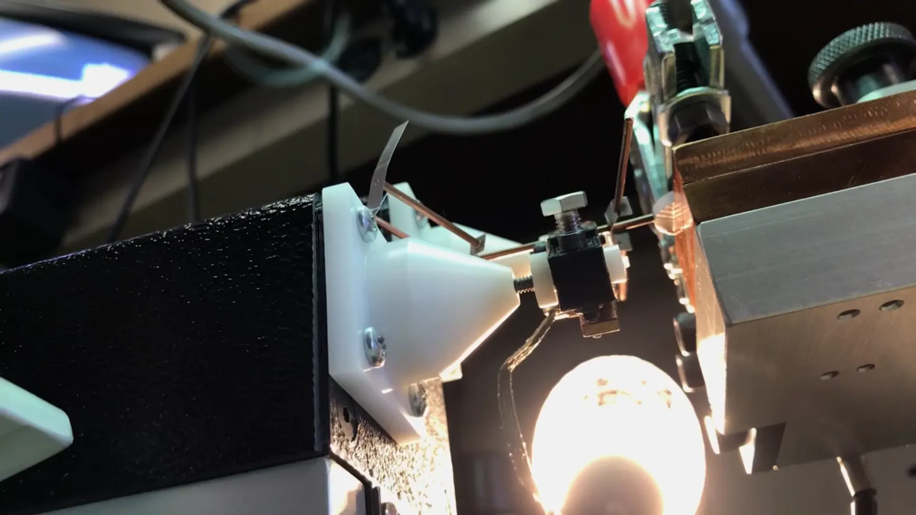Wire held between white electrode cones with a lamp glowing behind the fixture