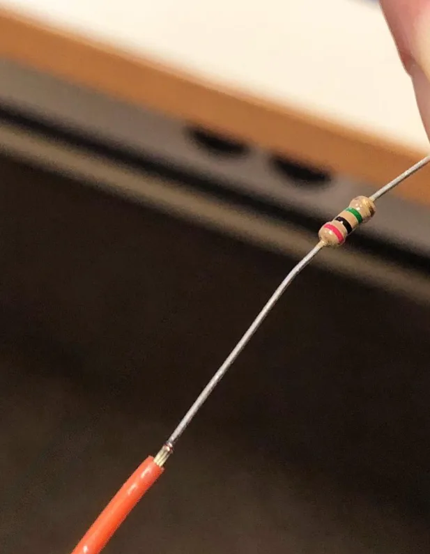 Orange insulated wire welded to a bare lead carrying a small resistor, held up for inspection